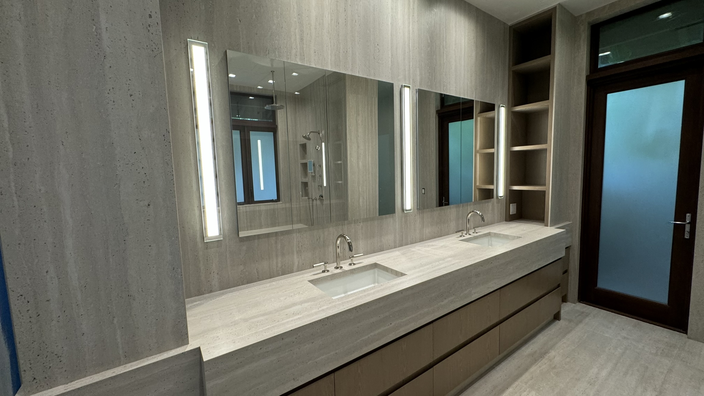 A closer look at the long countertop, wall-mounted faucets, mirrored cabinets and wood-toned vanity drawers.