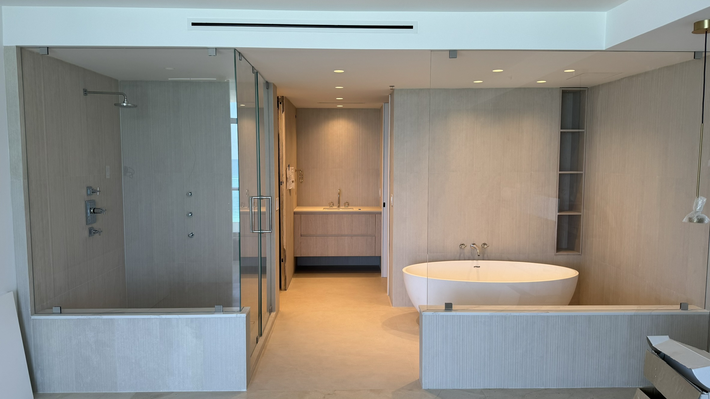 A freestanding bathtub beside a glass shower, with light finishes and recessed shelving.