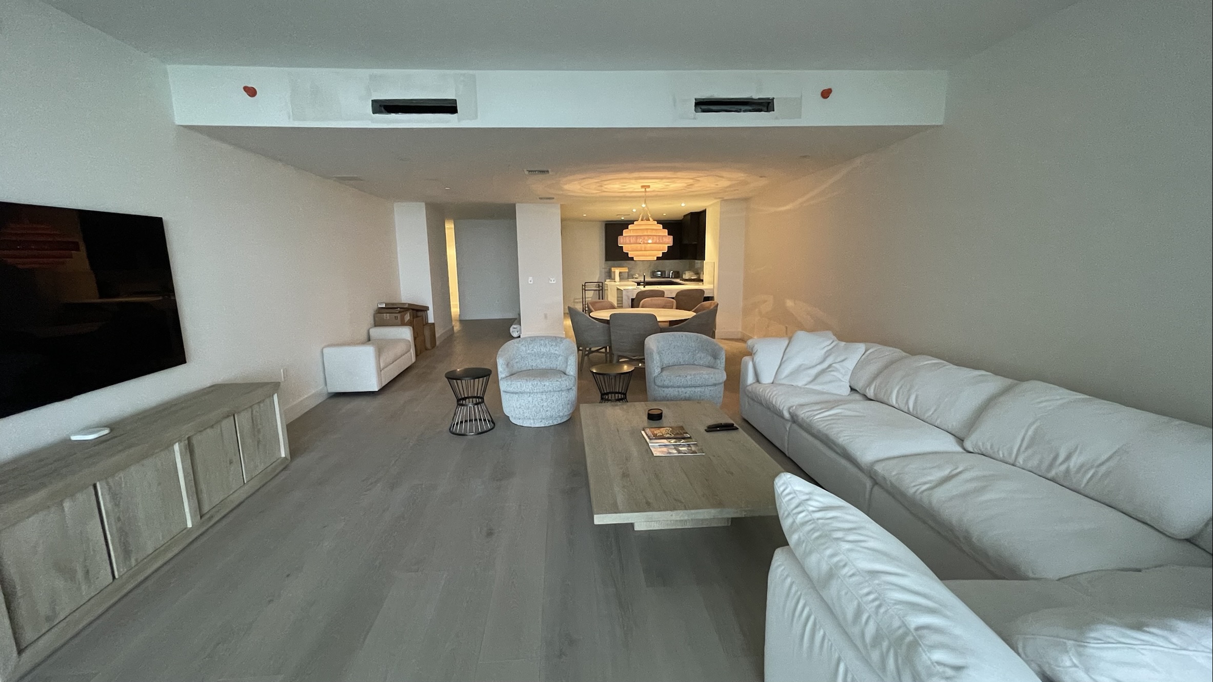 A continuous living and dining area with light flooring, a white sofa and a long media cabinet.