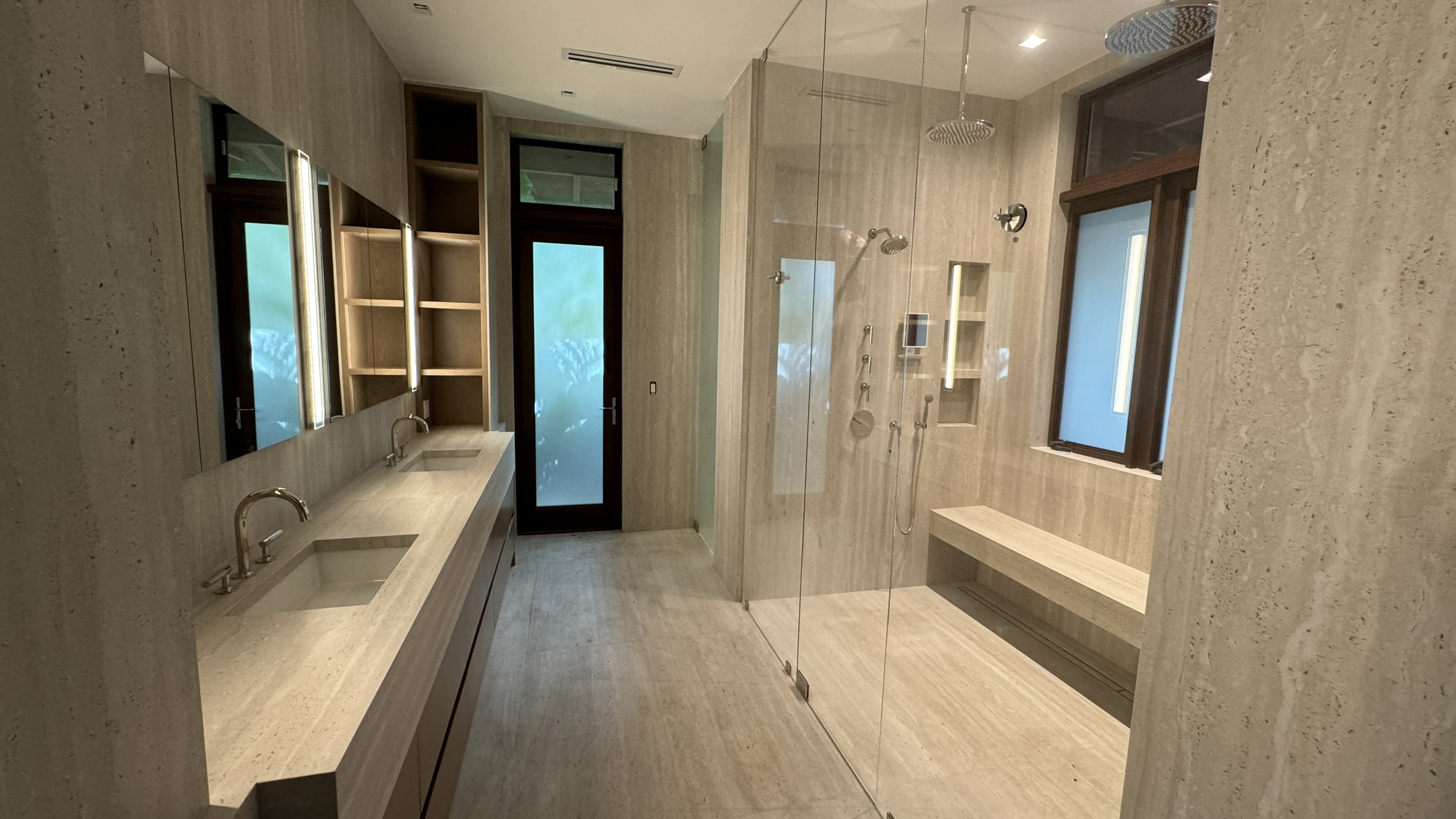 A long vanity, textured wall finishes and a glass-enclosed shower with a built-in bench.